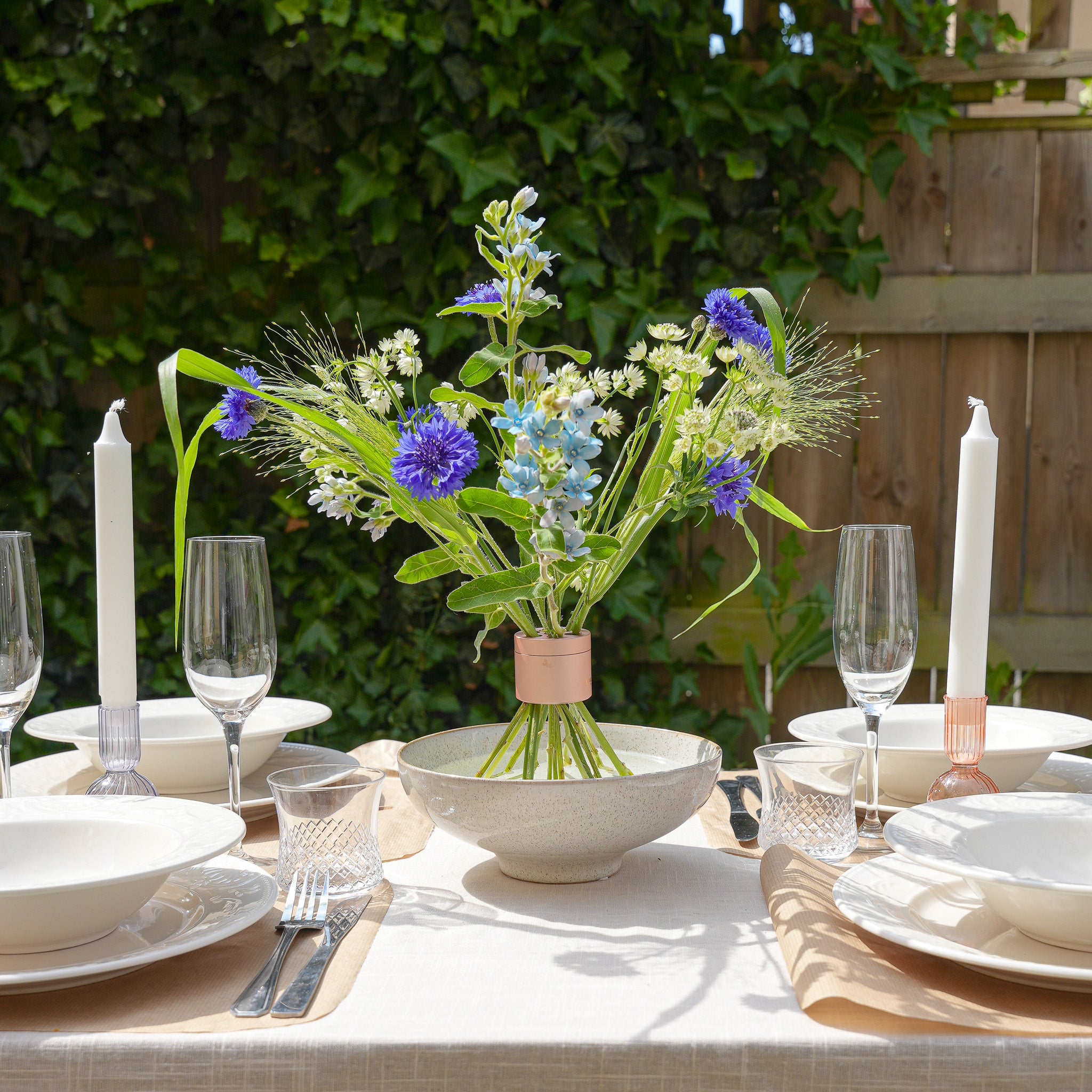 Dining table set with floral centerpiece inside a small hanataba pink champagne, candles, and glassware outdoors.