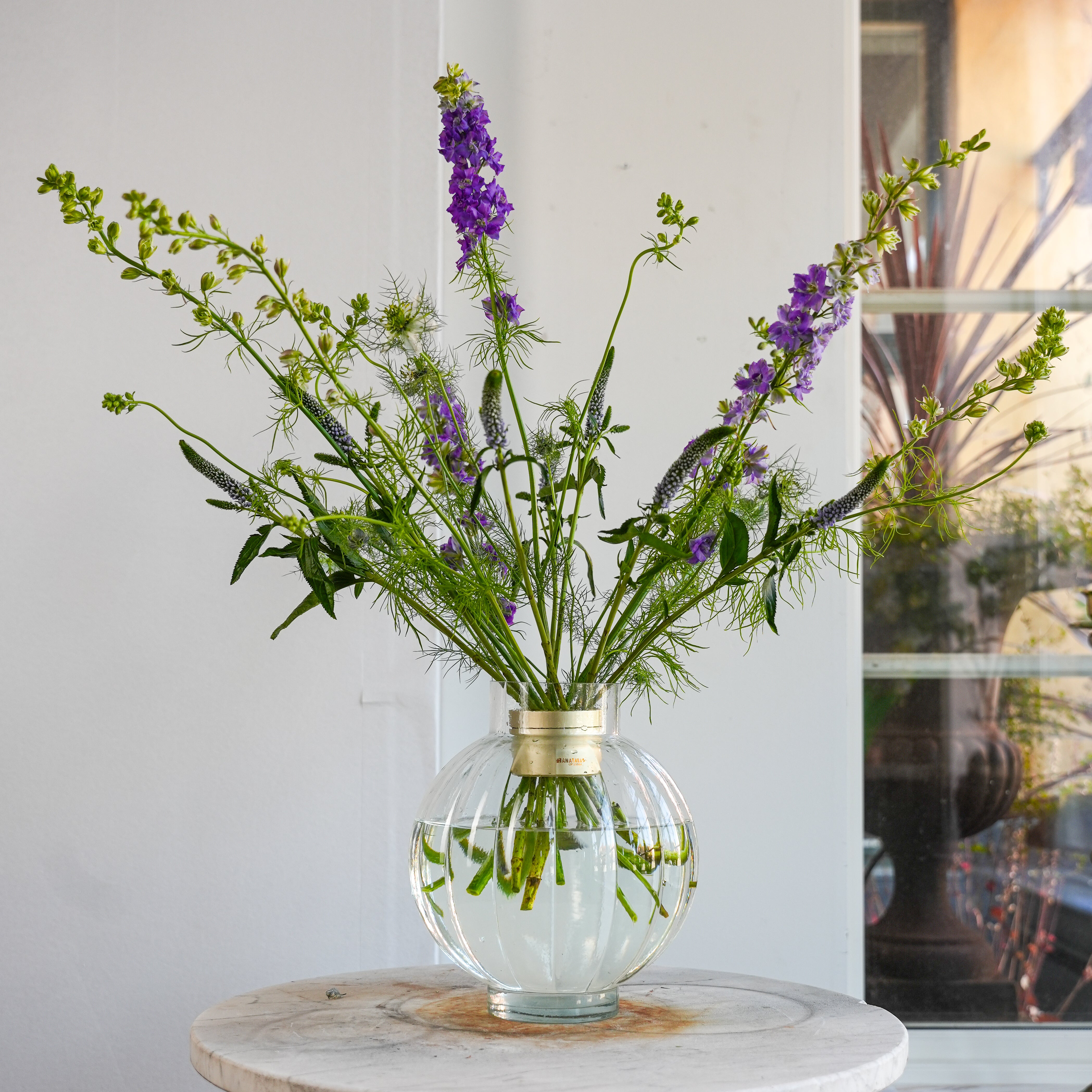 Clear vase with green and purple flowers in a champagne gold hanataba on a marble table