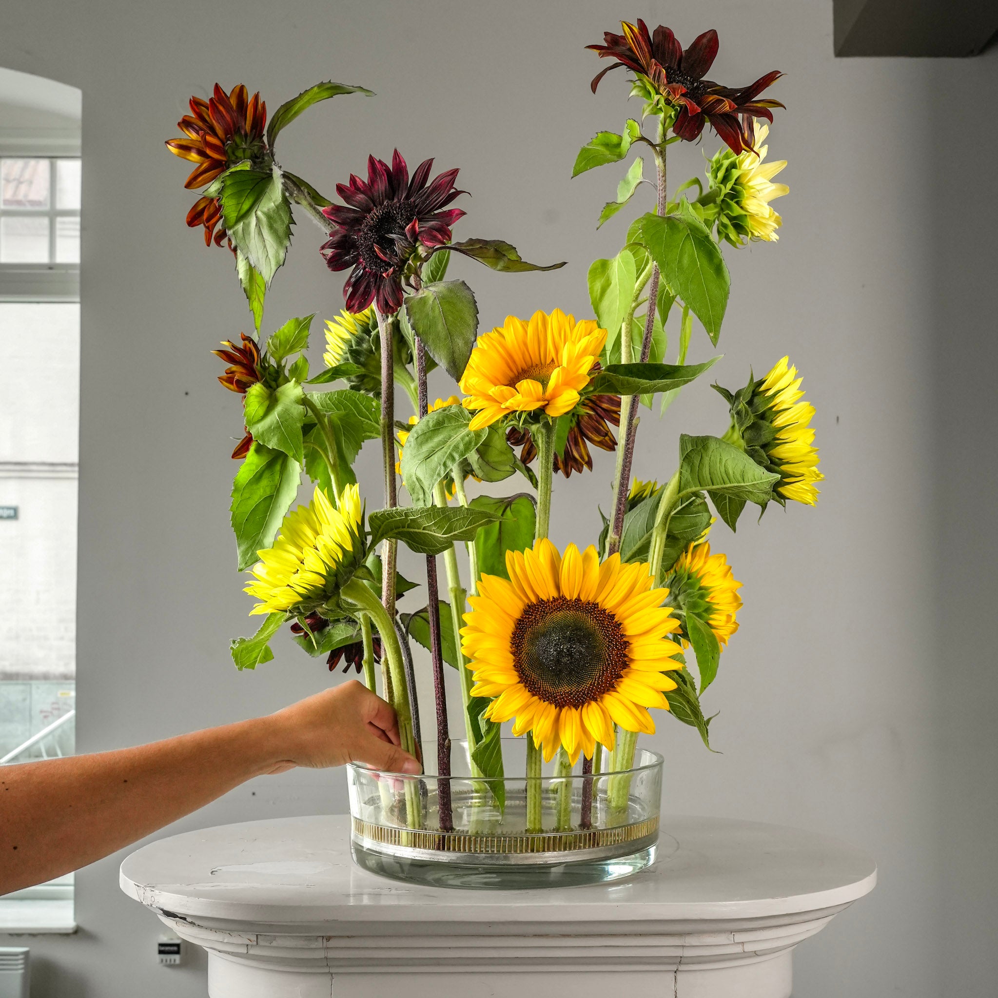 Bunch of sunflowers and other flowers on a hanataba kenzan ring 120 mm flower frog pin holder ring in a glass vase on a white surface.