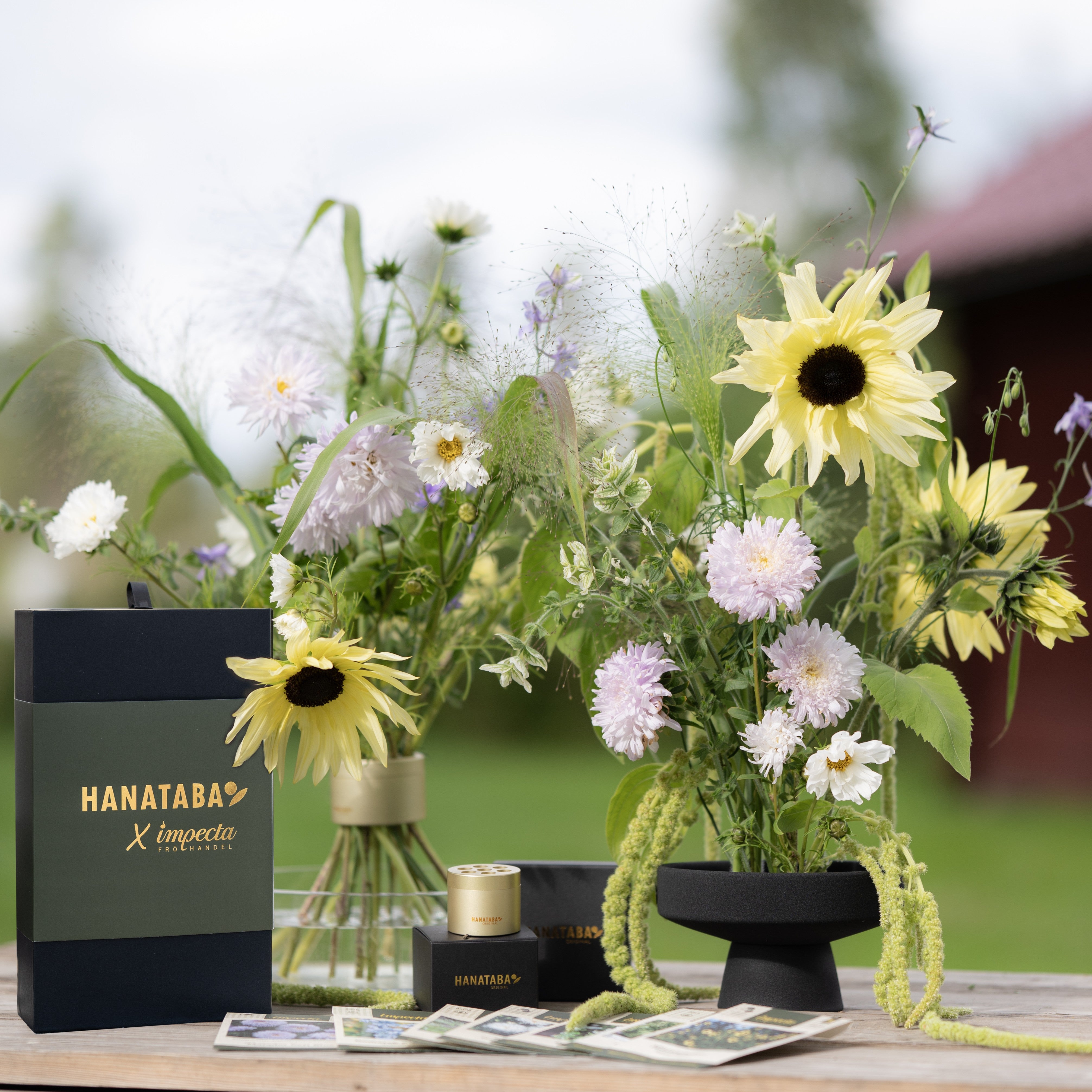 Floral arrangement with a black box labeled 'HANATABA X Impecta Fröhandel' on a wooden surface. For the 'Lumi' Gift Box Hanataba x Impecta Fröhandel