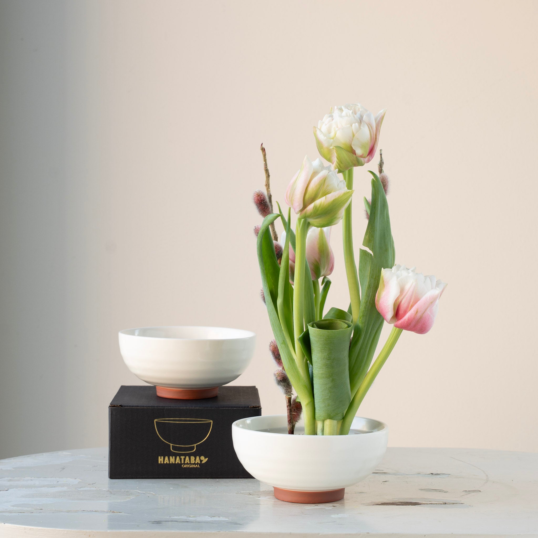 Floral arrangement in a white ceramic kenzan 'kobachi' bowl on a marble surface with a neutral background
