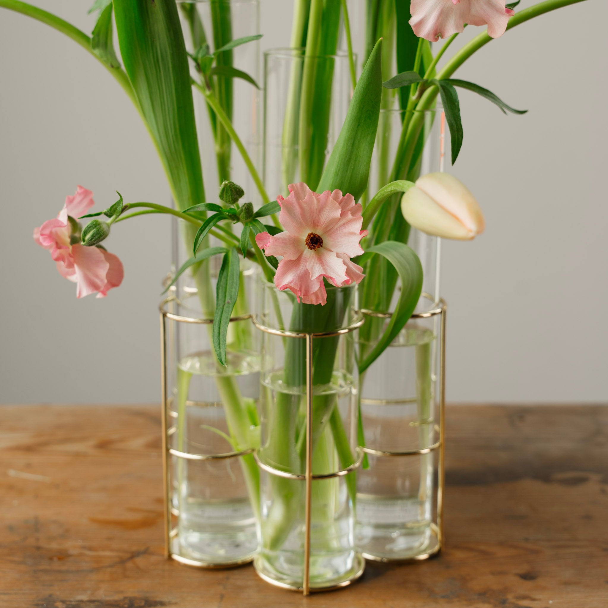 Clear glass vases with gold wire frames (LiSign Milano Vase) holding pink flowers on a wooden surface.