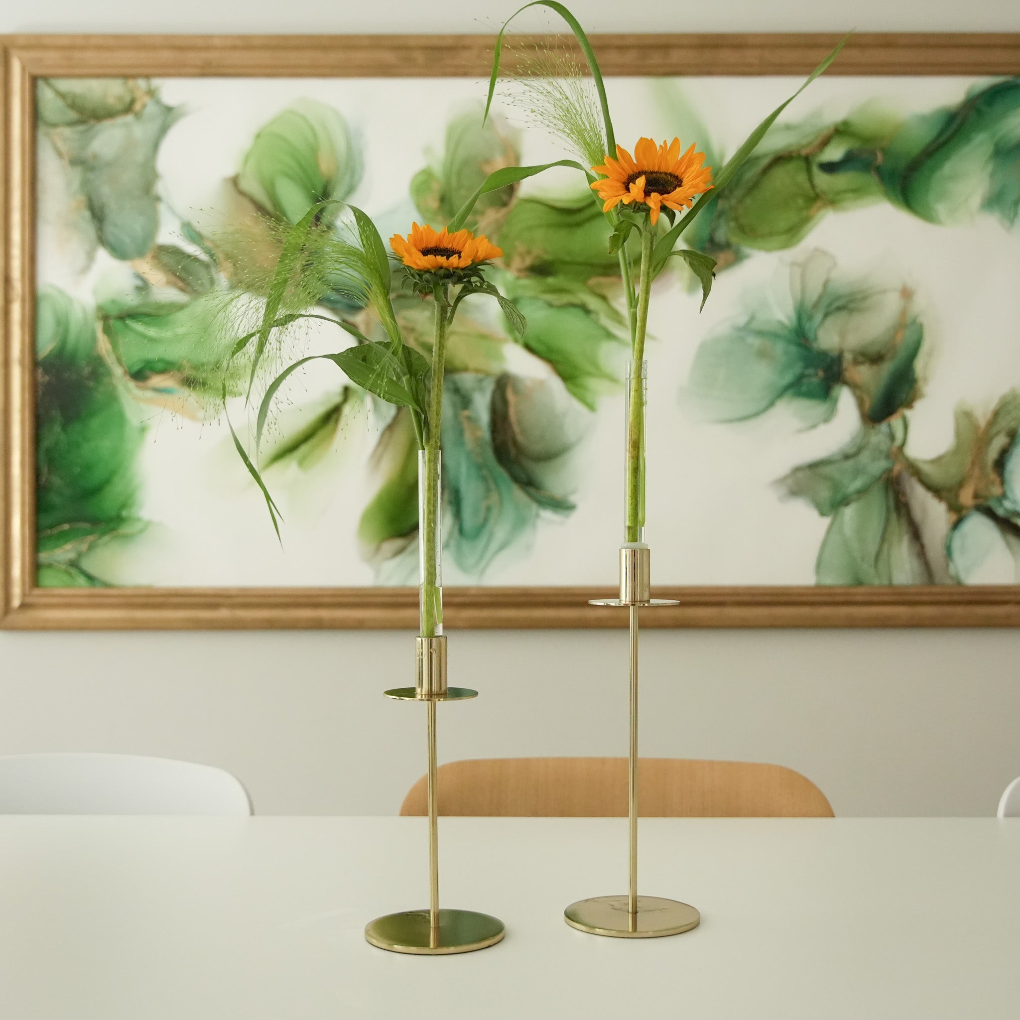 Two gold vases with sunflowers on a table in front of a decorative painting.