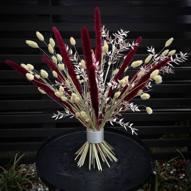 A vibrant ikebana arrangement of crimson and cream dried flowers in a Hanataba bouquet twister, set against a black slatted backdrop