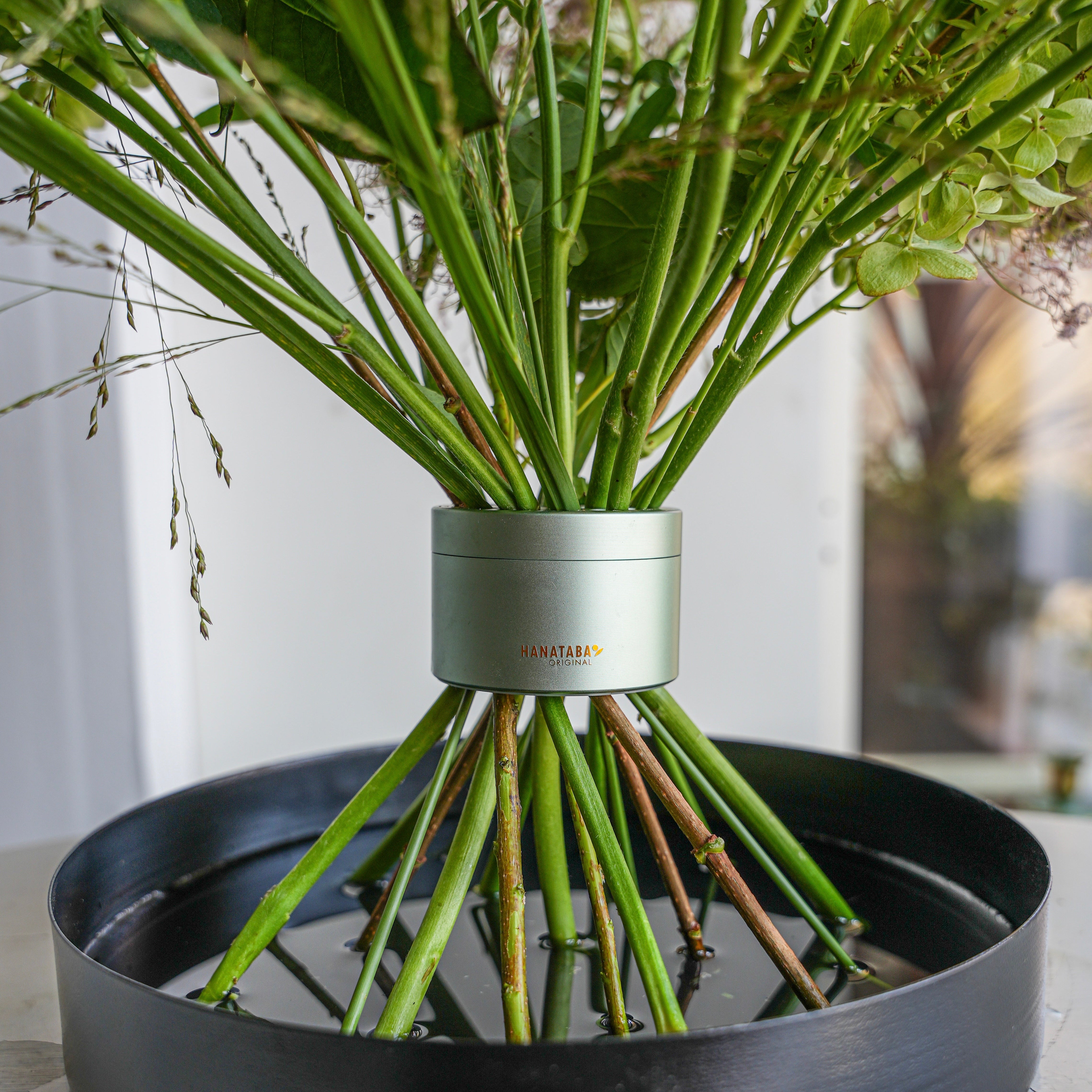 Flower stems arranged in a lush Ikebana bouquet on a black floral tray filled with water.