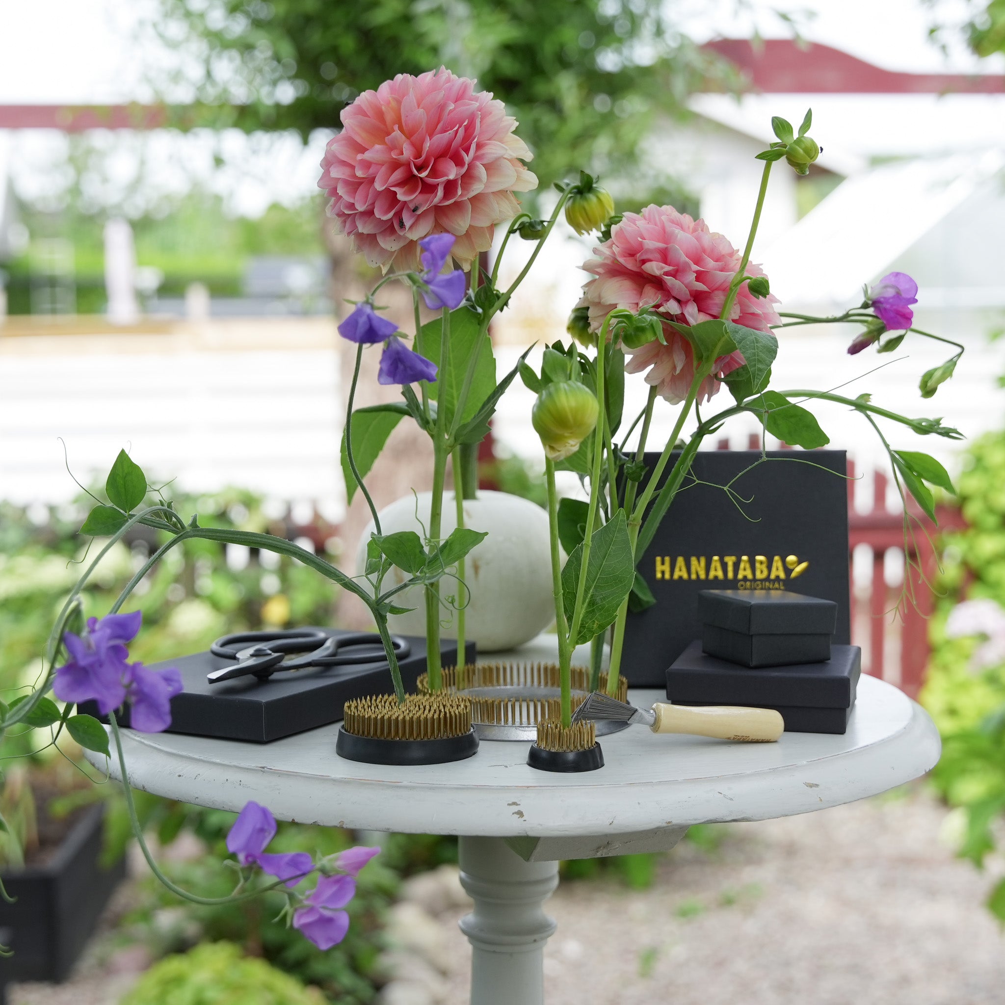 Table with Hanatabas exclusive flower frog trio and tool set, containing kenzan flower frog 34 mm, kenzan flower frog 70 mm, kenzan flower frog ring 120 mm, a kenzan cleaning brush and a japanese scissor for ikebana inspired flower arrangements