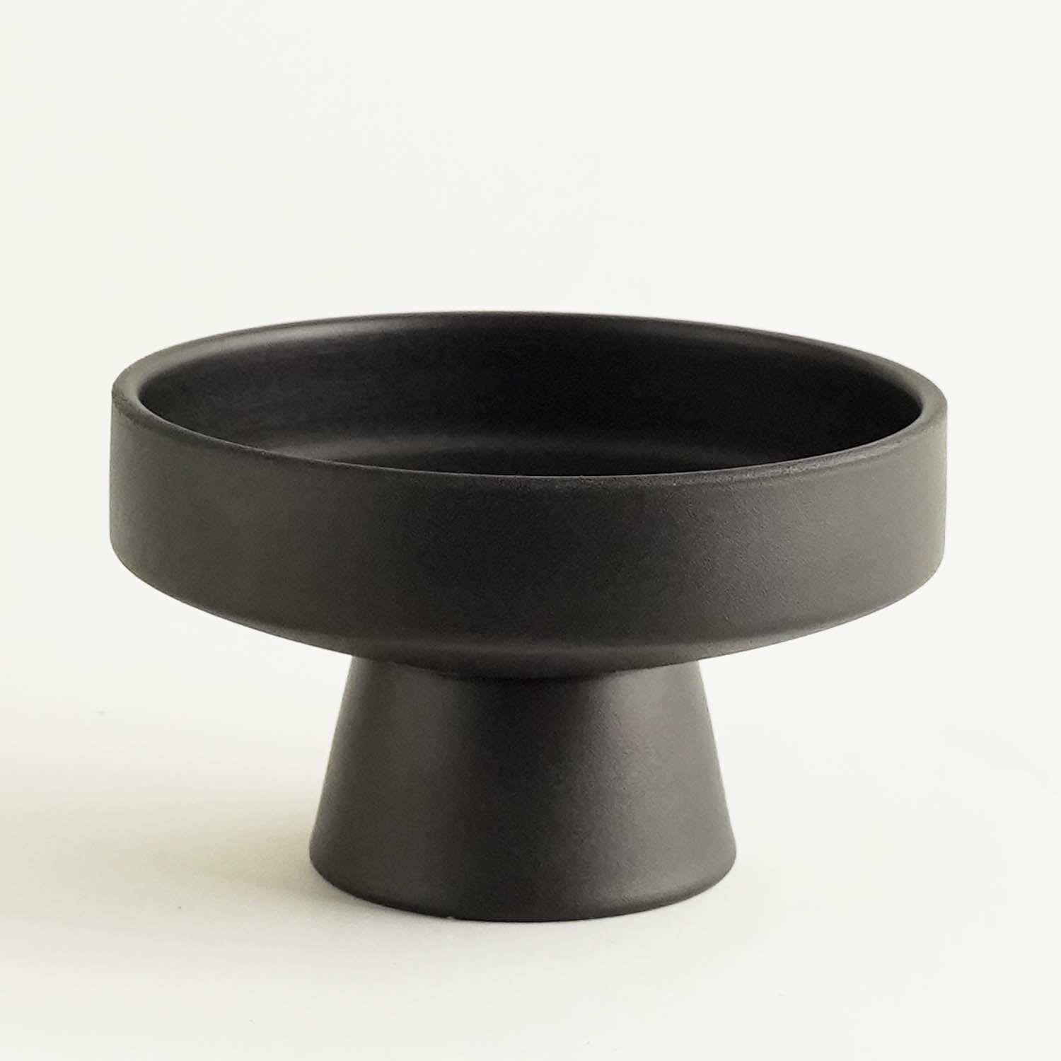 A black ceramic bowl, minimalist in scandinavian design, features a wide, shallow top and a narrow, cone-shaped base resembling an ikebana vase. Its elegantly set against a plain white background.