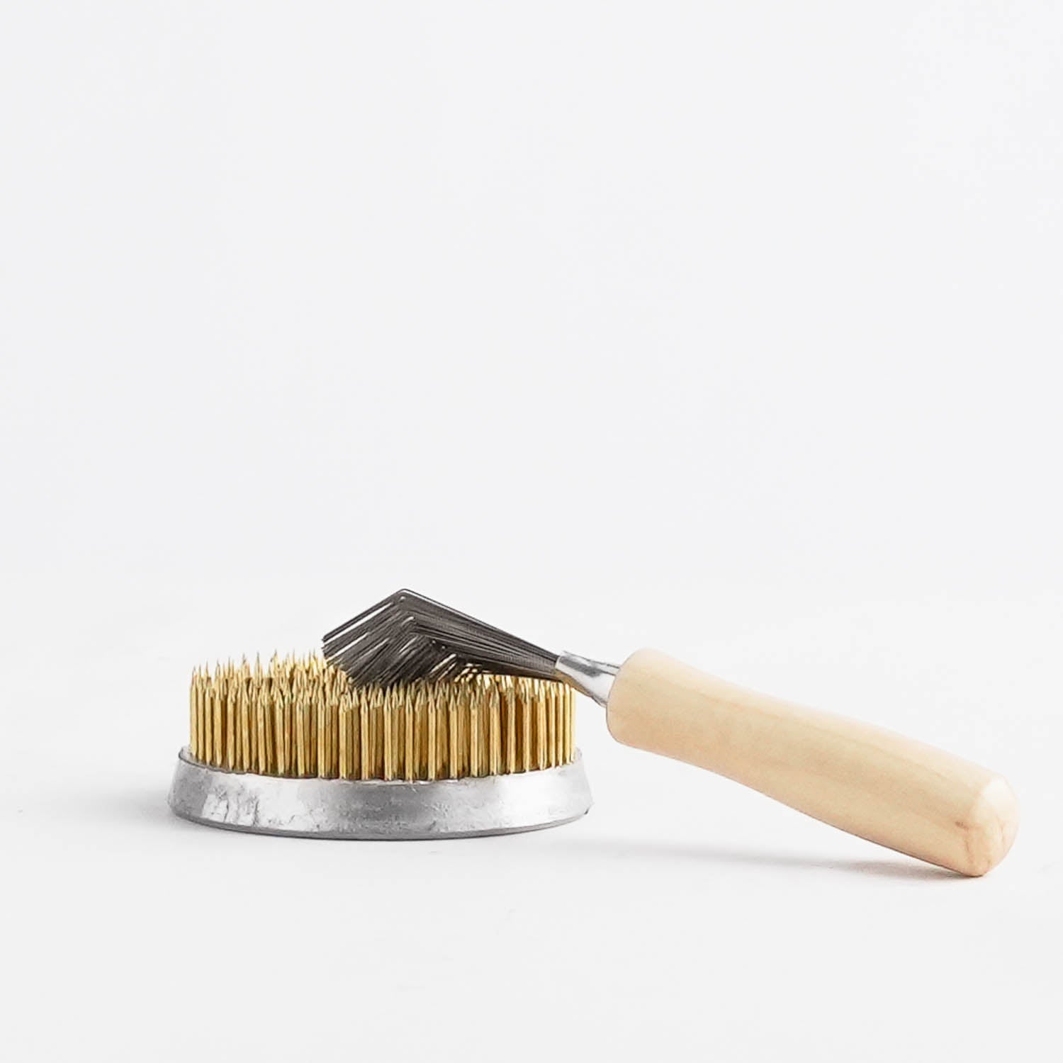 A comb-like kenzan rake, cleaning tool, with a wooden handle on top of a flower frog, on a white background.