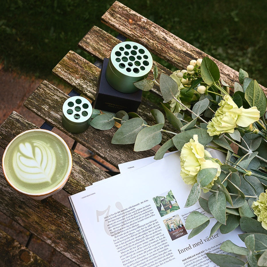 Eucalyptus and a cup of matcha tea next to the Hanataba bouquet twister tool on a wooden table in a garden setting.