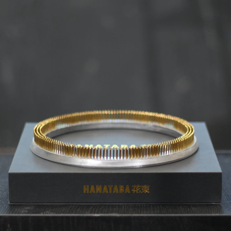 A gleaming 200mm Kenzan ring rests atop a sleek gray presentation box with the gold inscription "HANATABA 花束," showcasing elegance and functionality in floral arrangement.
