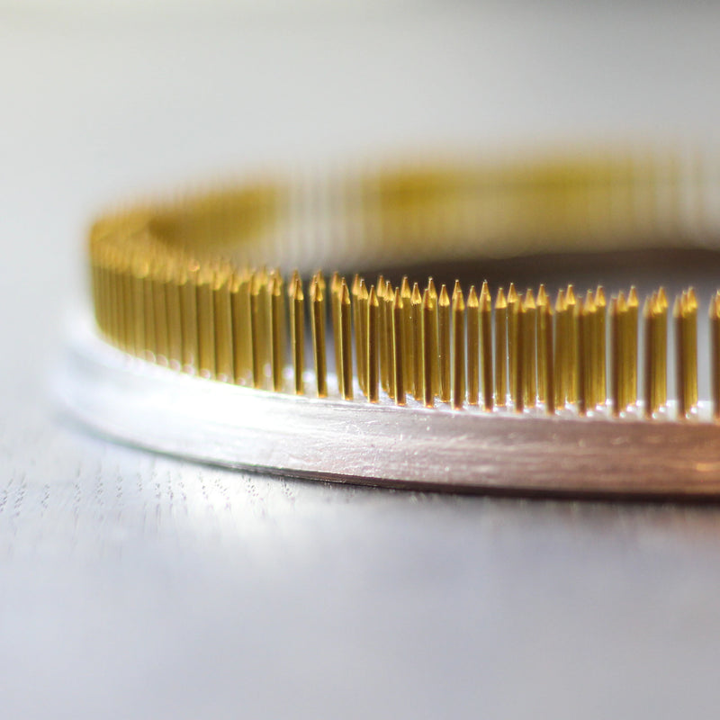 Close-up of a 200mm golden Kenzan ring against a soft-focus background, its numerous fine spikes glinting in the light, ready for elegant floral arrangements.