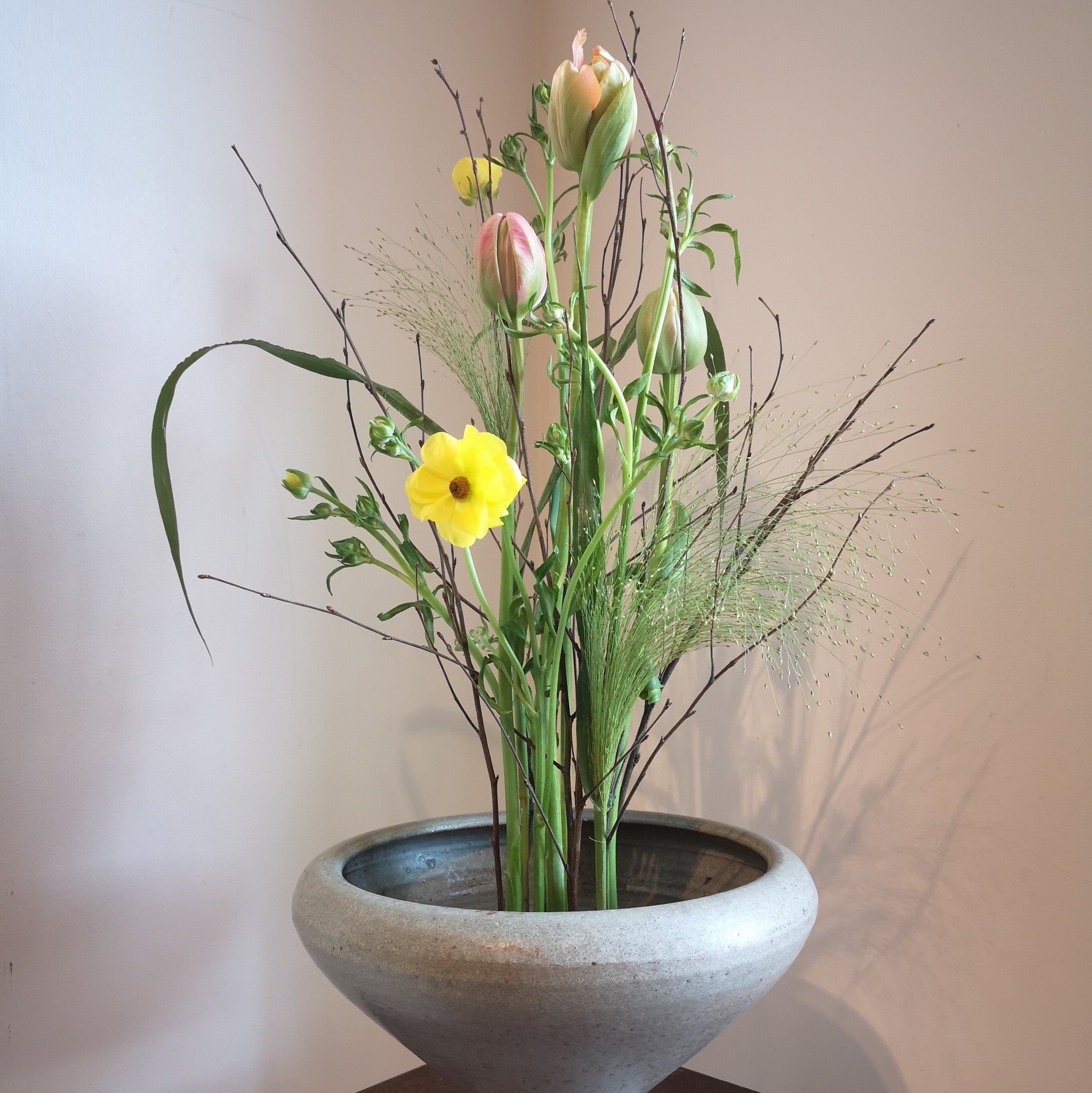 A serene floral display with a yellow daffodil and soft pink tulips, all secured by a 70mm Kenzan ring in a stone bowl.