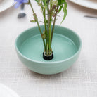 Small green ceramic bowl with a plant on a Hanataba Magnetic Mini Kenzan on a light fabric background