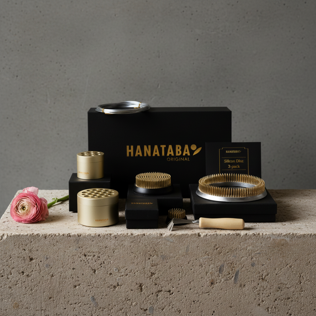 Hanataba flower design set including, hanataba kenzan 34 mm, kenzan 70 mm, kenzan ring 120 mm, Hanataba bouquet twister flower holder champagne gold with 3 silicon discs, bonsai wire 2 mm silver with a pink ranunculus flower on a gray surface