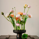 Floral arrangement in a black hanataba ceramicikebana vase on a wooden surface with a neutral background