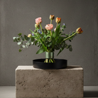 Bouquet of flowers in a black metallic vase on a concrete block with a gray background