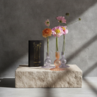 Hanataba Candle Vase. Three small glass vases with flowers on a stone surface against a gray wall.