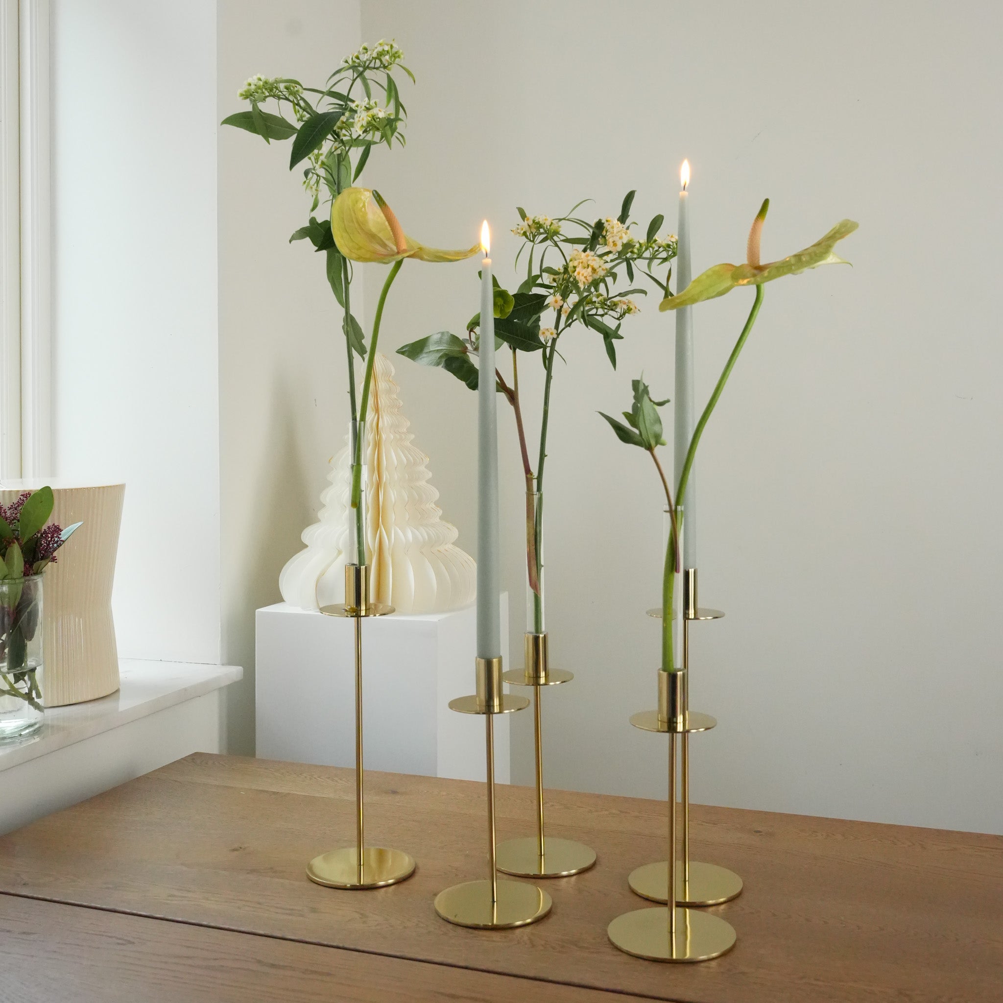 Hanataba candle Vase 3-pack in three gold candle holders with flowers on a wooden surface against a white wall