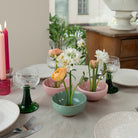 Dining table setting with floral arrangements in small ceramic kenzan 'kobachi' bowls, candles, and glasses.