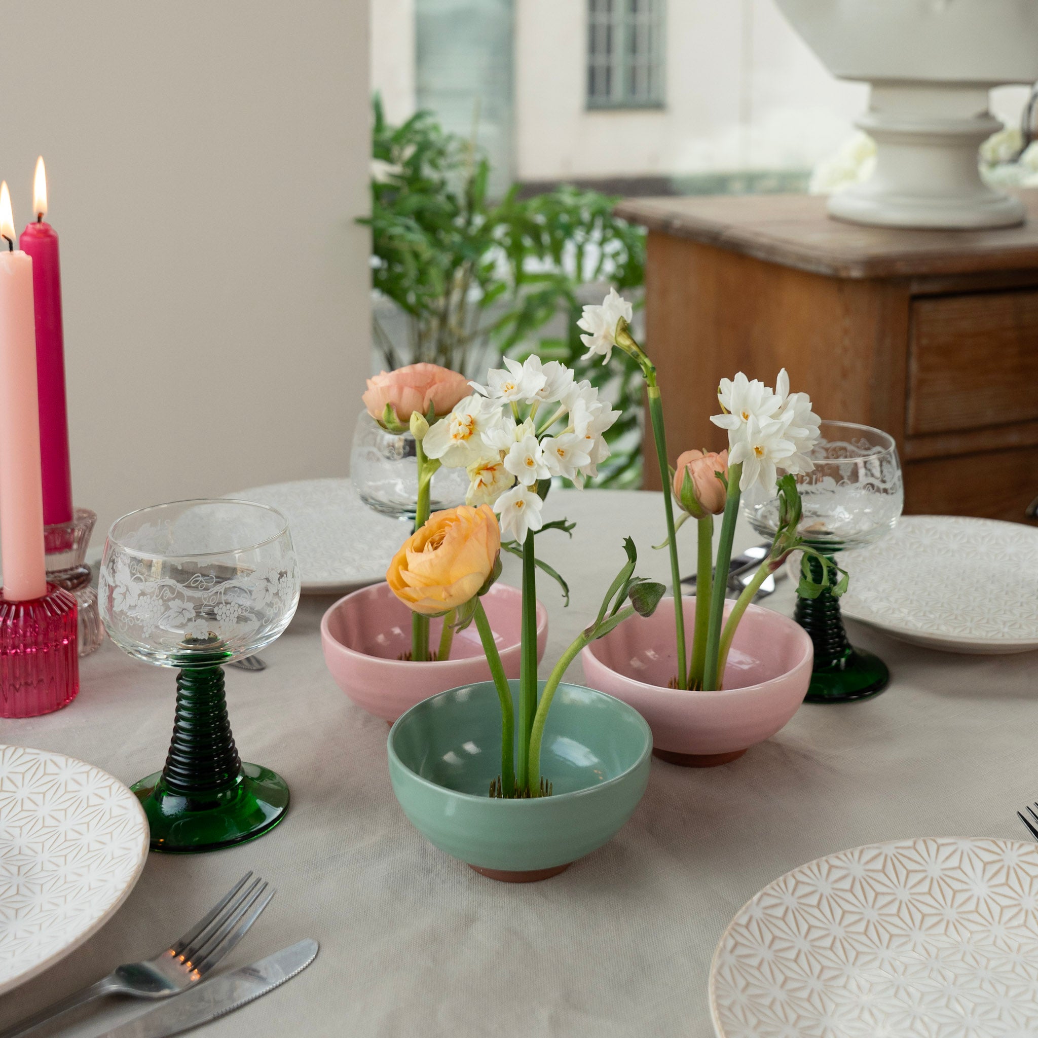 Dining table setting with floral arrangements in small ceramic kenzan 'kobachi' bowls, candles, and glasses.