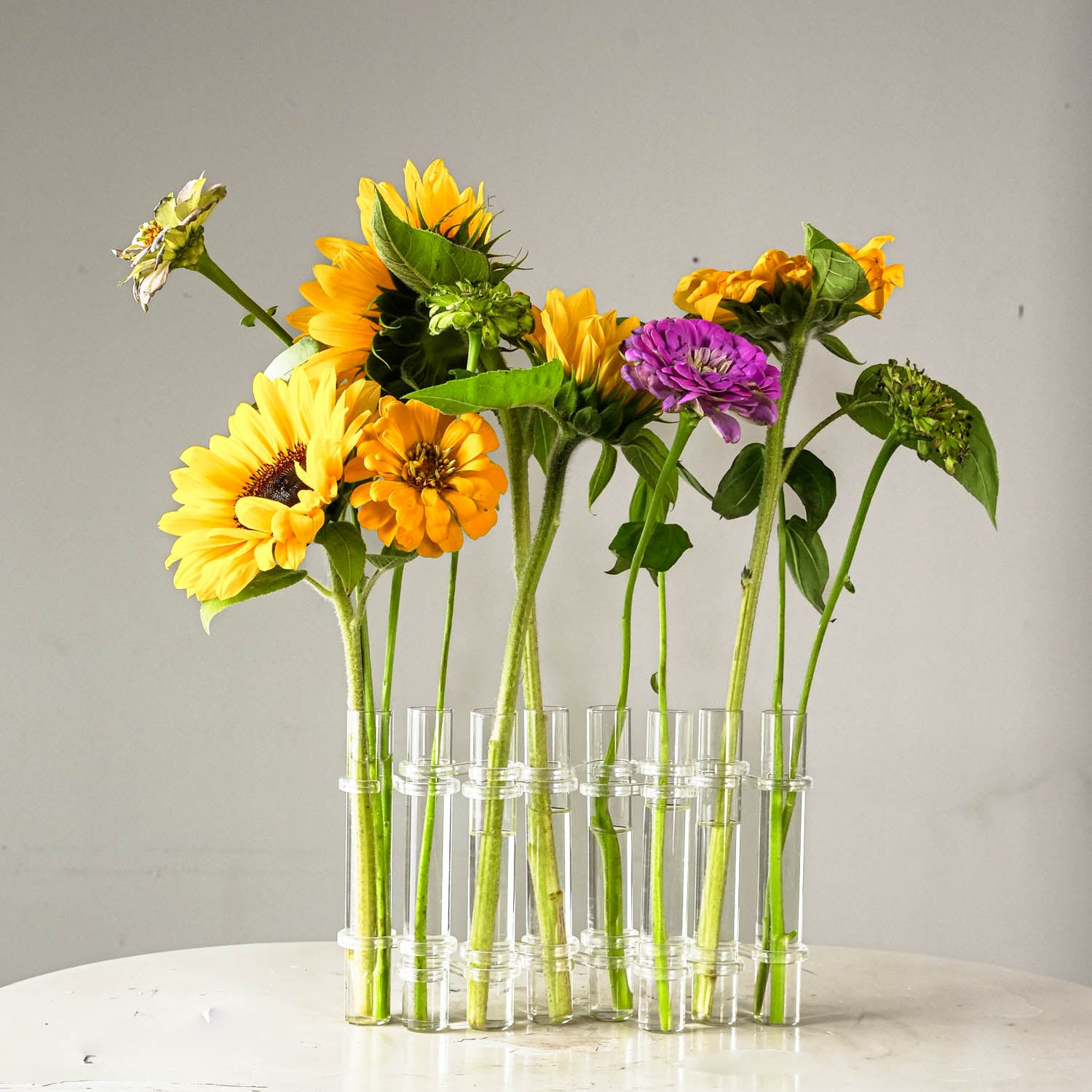 Clear glass flower flute with sunflowers and a purple flower on a gray background