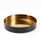 A round metal tray with a brushed gold interior and a matte black exterior, photographed on a clean white background.