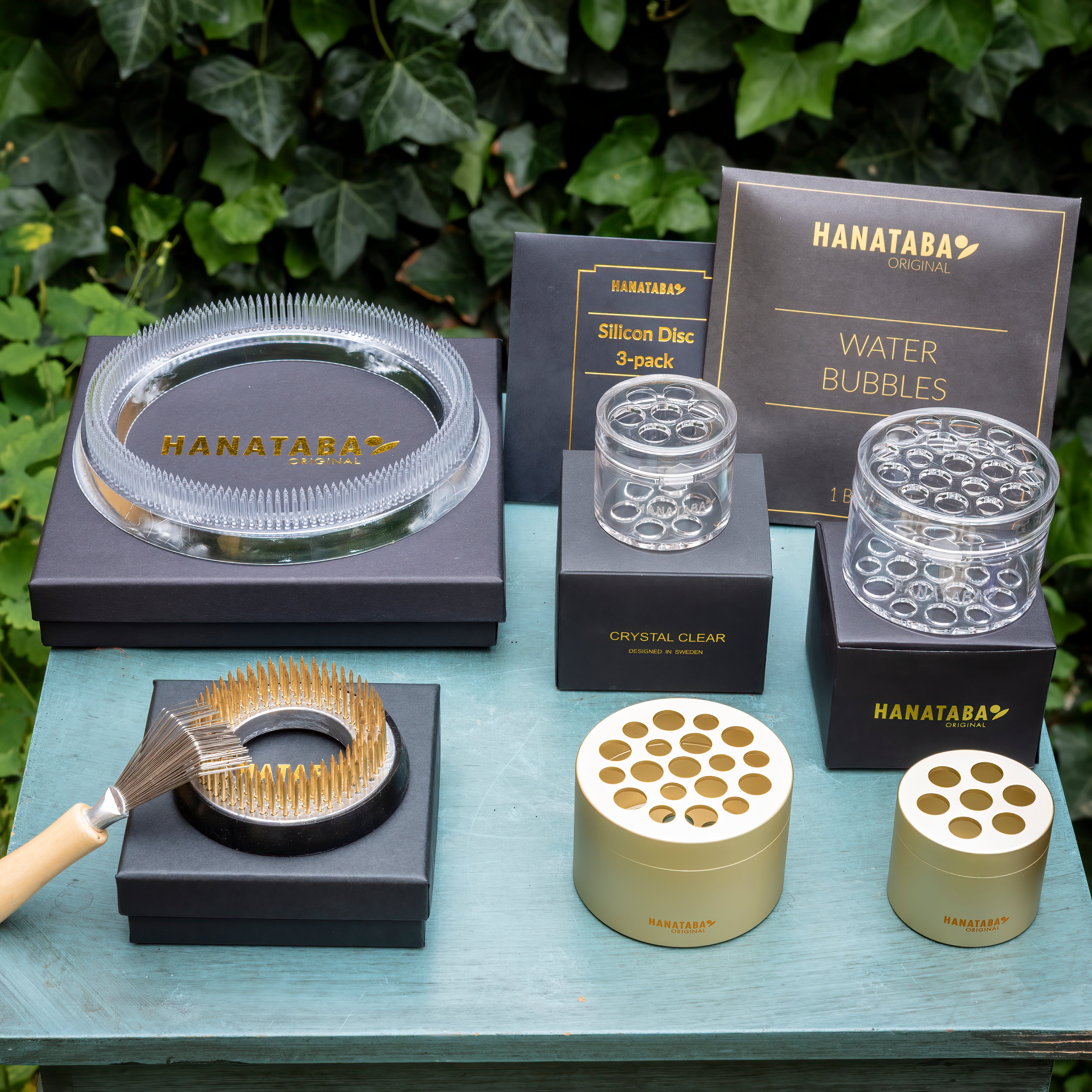Collection of Hanataba flower arrangemnt tools and products on a table with greenery in the background.