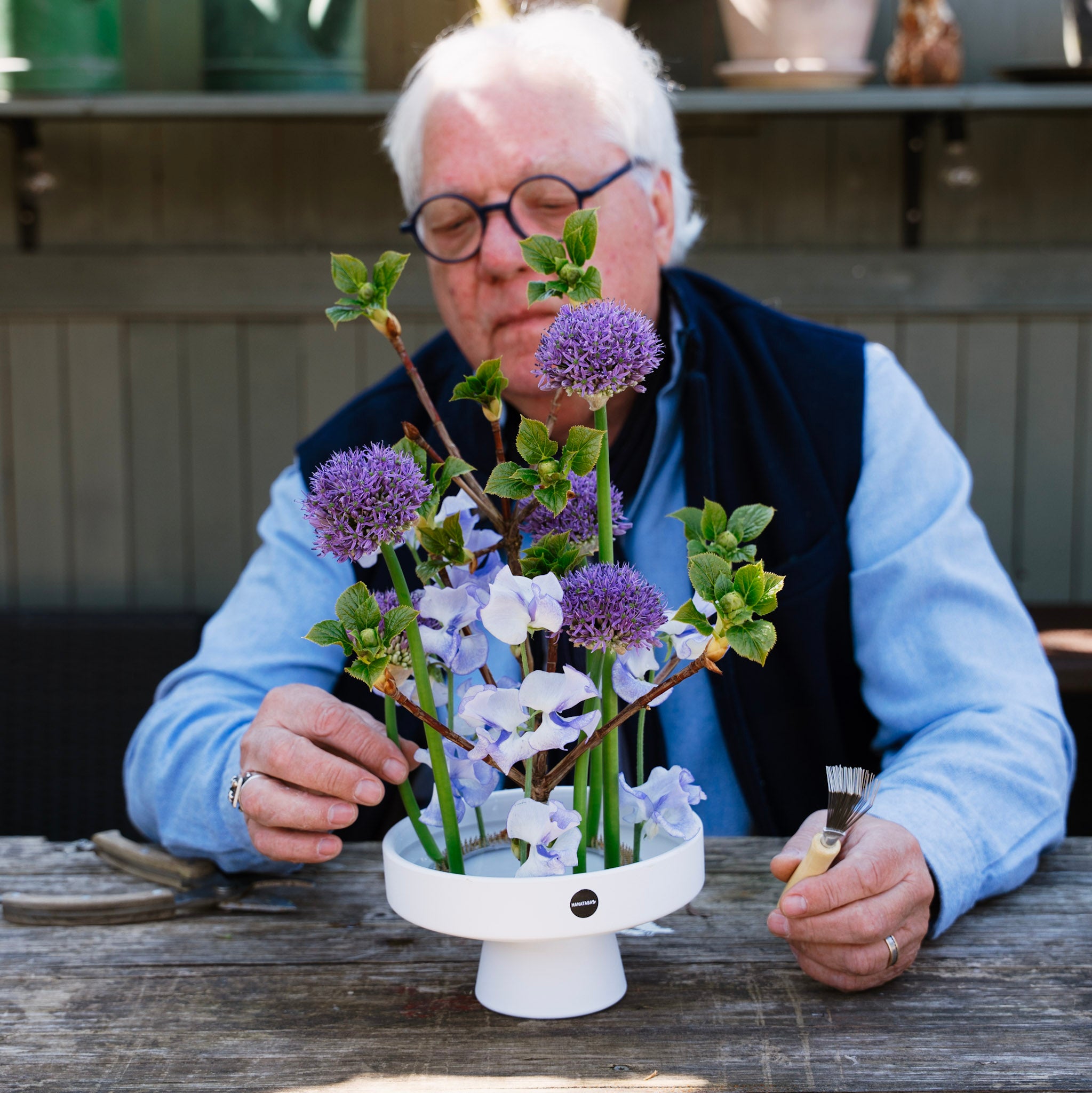 Person arranging flowers on a wooden table outdoors