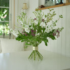 Bouquet of white and purple flowers with green leaves in a Hanataba Bouquet flower twister stem holder on a white surface.