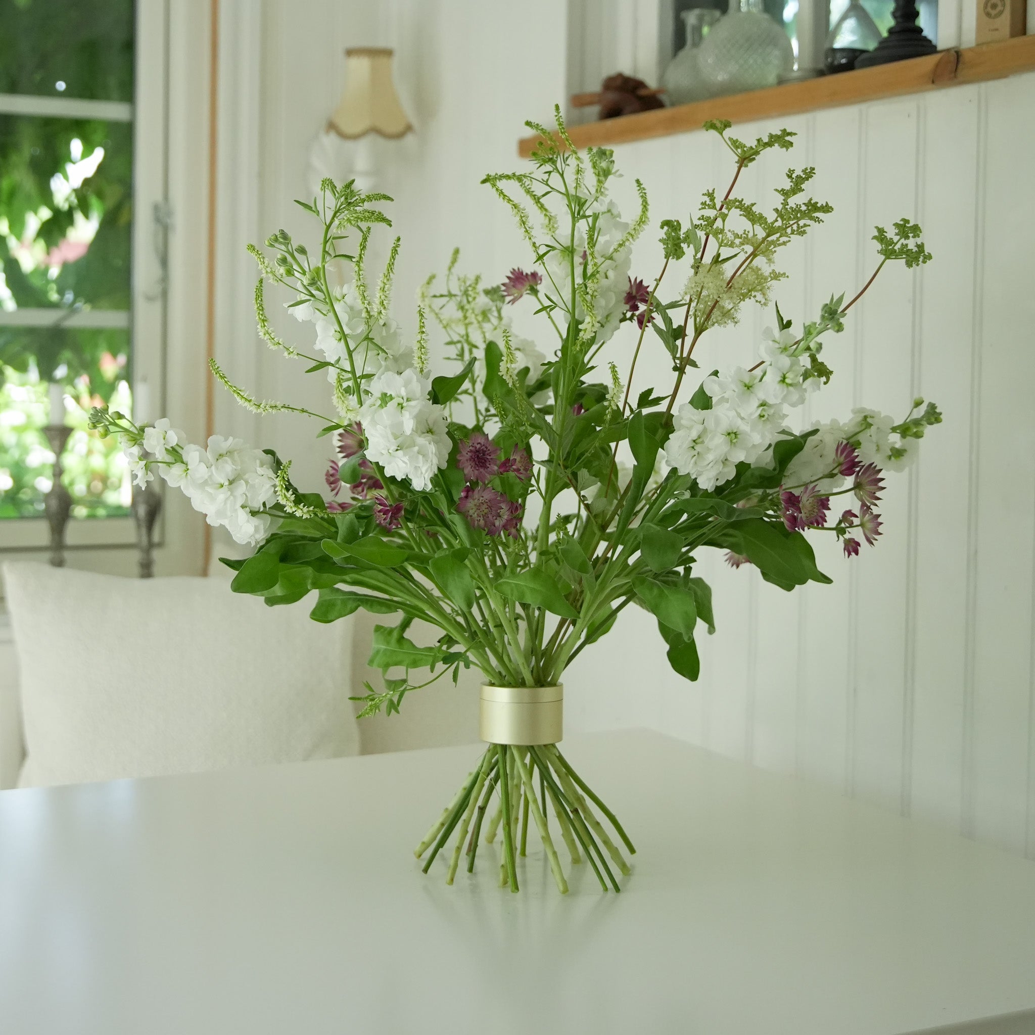 Bouquet of white and purple flowers with green leaves in a Hanataba Bouquet flower twister stem holder on a white surface.