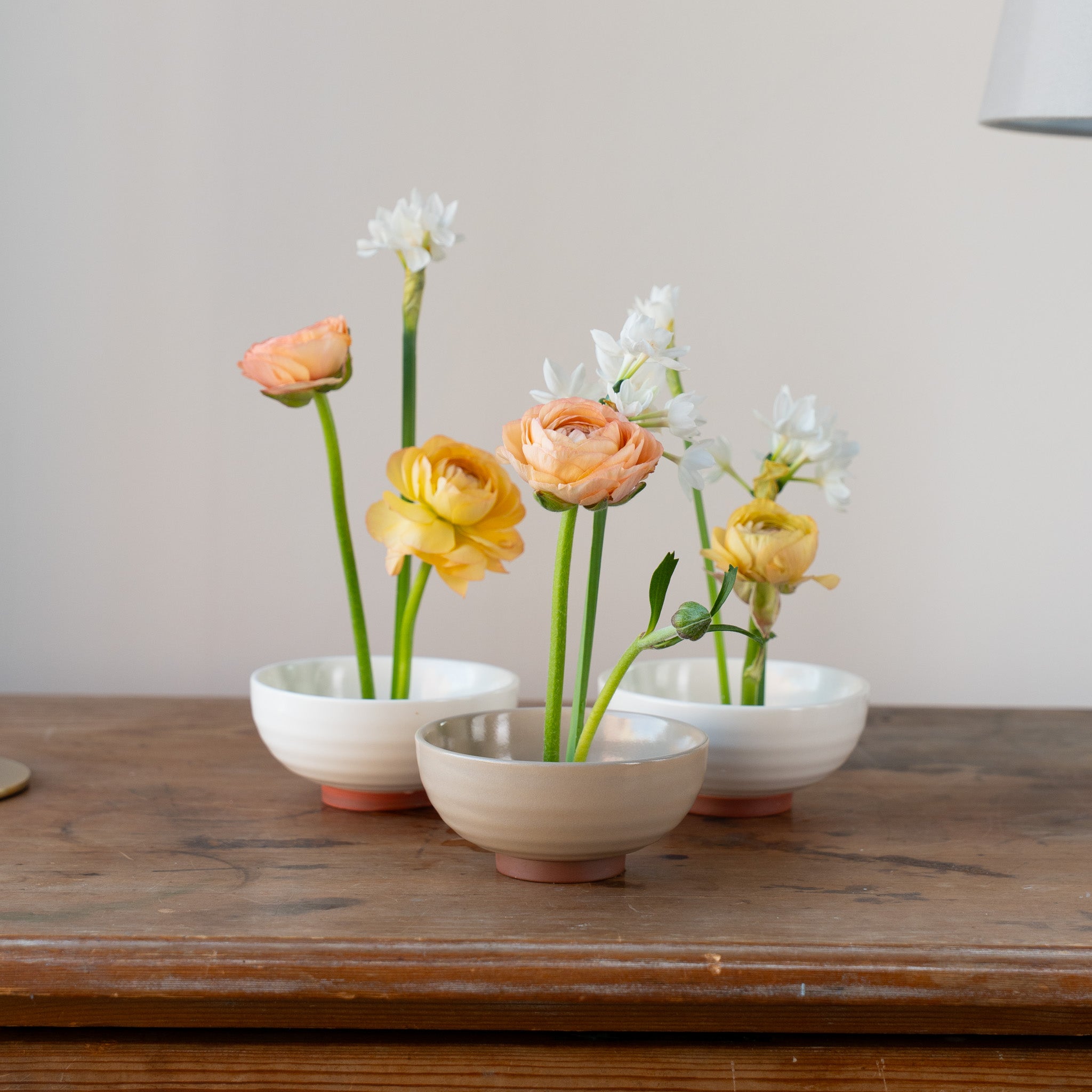 Three small hanataba ceramic kenzan 'kobachi' bowls in white and beige colors with flowers on a wooden surface