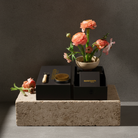Decorative setup with flowers, grooming tools, and a black box on a concrete block against a dark background.