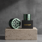 Green cylindrical Hanataba bouquet flower twisters and black box with 'HANATABA' branding used to create and make beutiful bouquets without previous experience, standing on a concrete block against a gray background.
