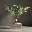 Bouquet of white flowers with green leaves inside a hanataba bouquet twister flower holder standing on a concrete block against a dark background