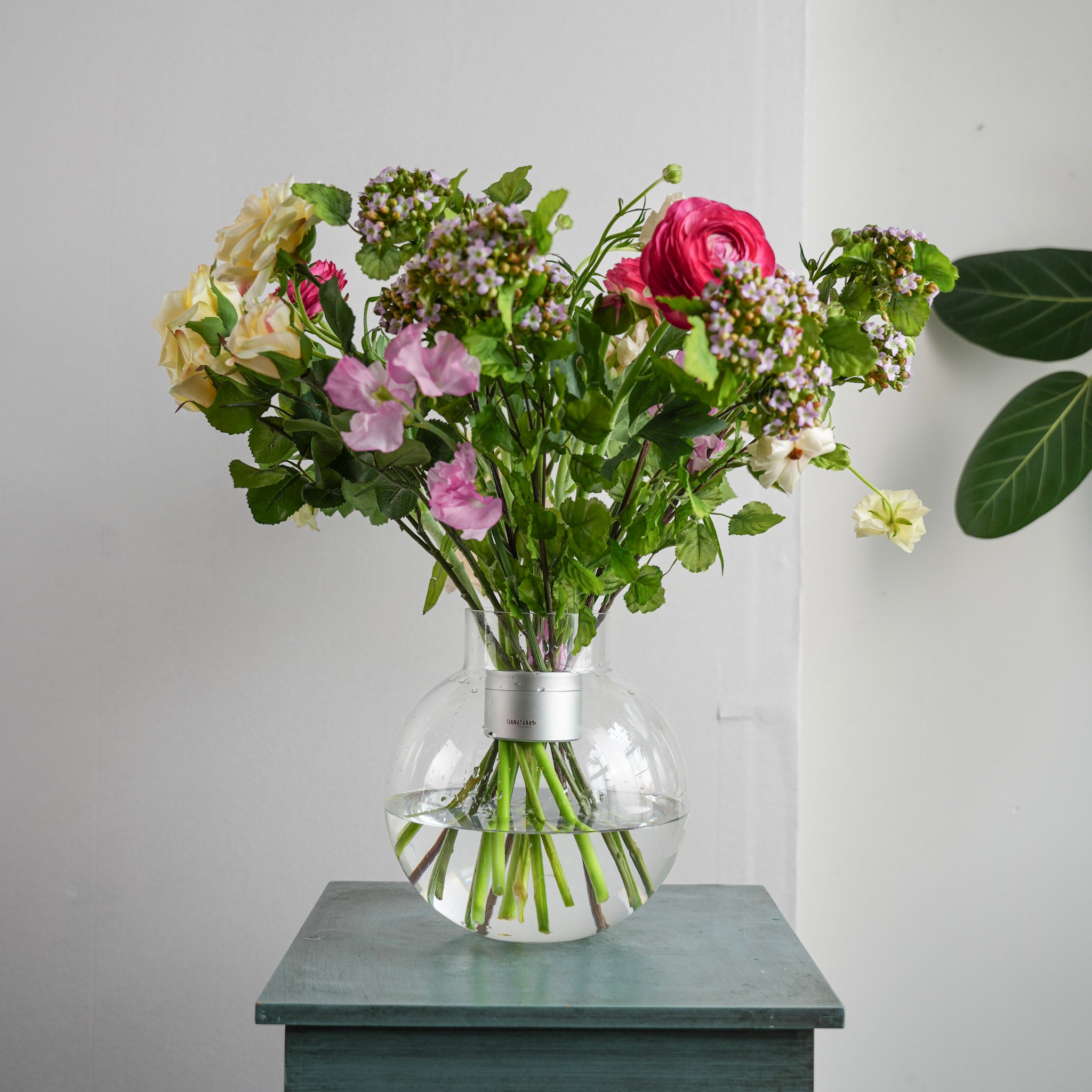 Bouquet of flowers inside a hanataba bouquet twister 'Pearly Silver' in a clear vase on a wooden surface with a light gray background