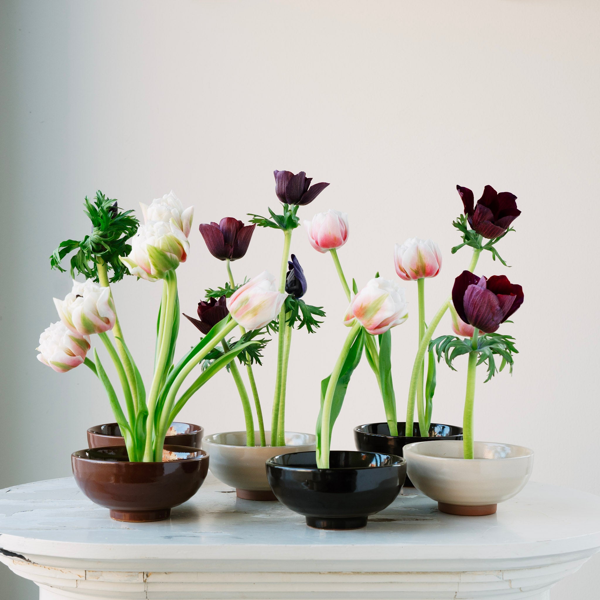 Floral arrangement in various small ceramic kenzan 'kobachi' bowls on a white surface with a light gray background