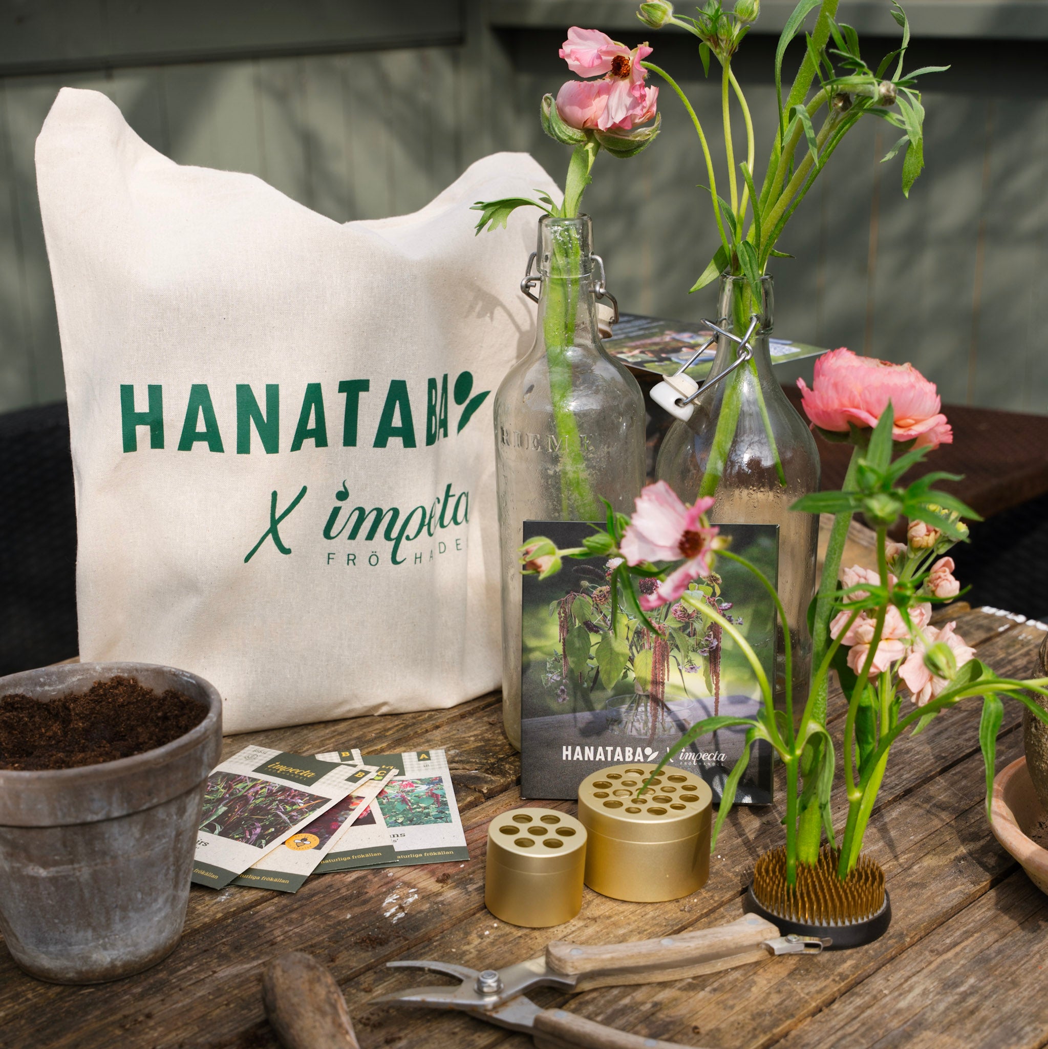 Gardening tools and plants on a wooden table with a 'HANATABA' bag.