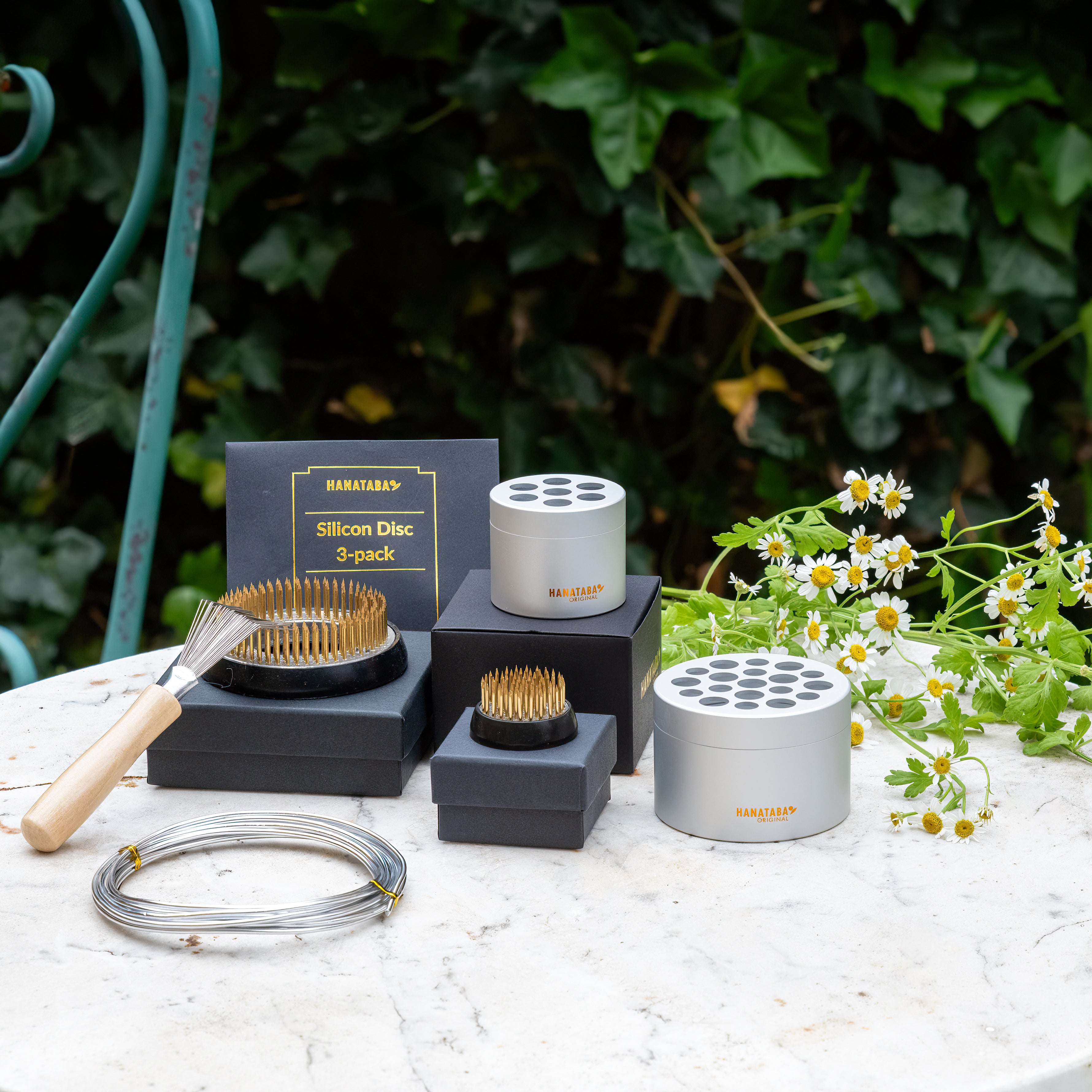 Collection of Hanataba gardening tools including kenzan, kenzan ring, Hanataba Bouquet Flower Twister, and other tools and accessories on a table with a natural background.