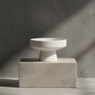 White ceramic bowl on a concrete block against a gray concrete wall