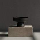 Black ceramic vase on a concrete block against a dark gray background