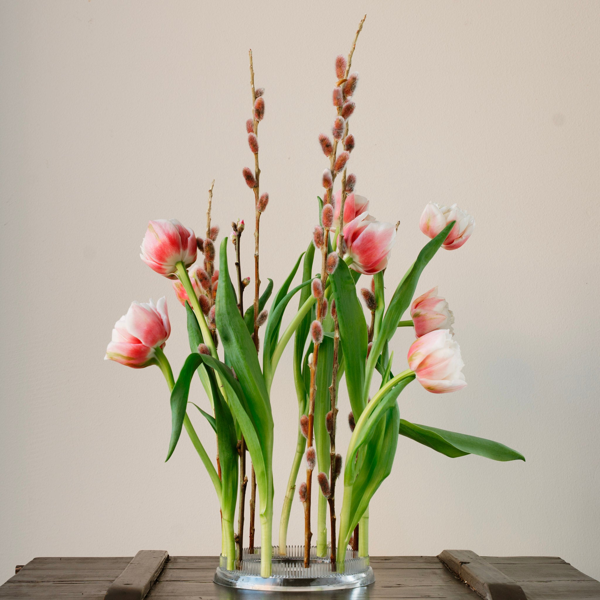 Floral arrangement with pink tulips and green leaves in a transparent Flower frog kenzan ring in 150 mm outer diameter on a wooden surface.