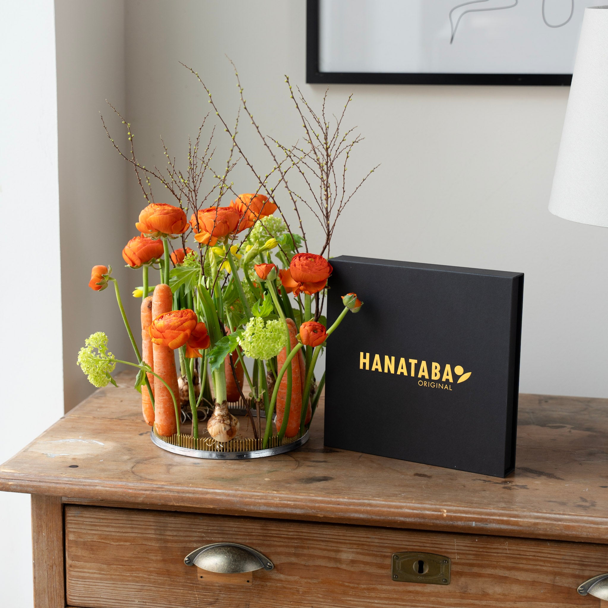 Floral arrangement in a kenzan ring 200 mm on a wooden surface with a black box labeled 'HANATABA' in the background.