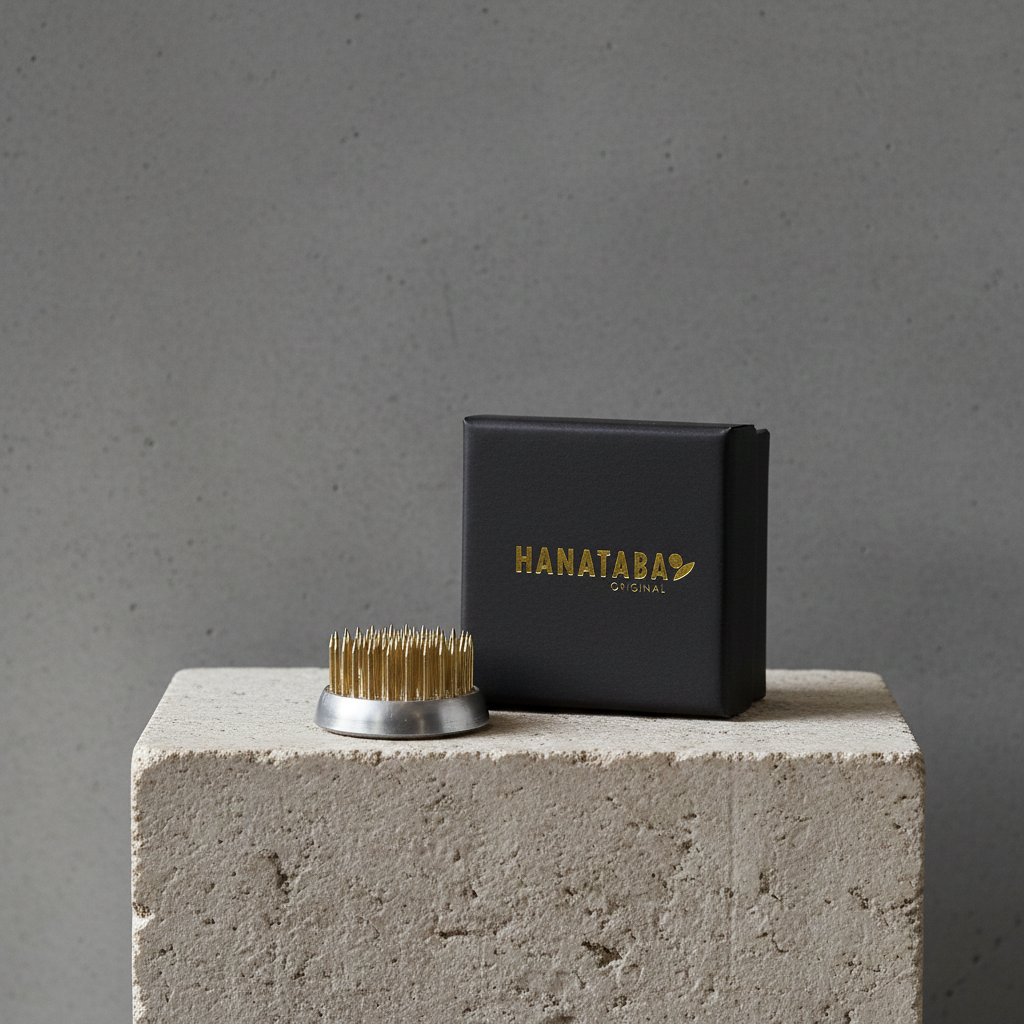 Kenzan flower frog 34 mm and black box with 'HANATABA' branding on a concrete block against a gray background