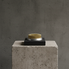 Small round kenzan ring 70 mm with gold and silver design on a black base, placed on a concrete block against a gray background.