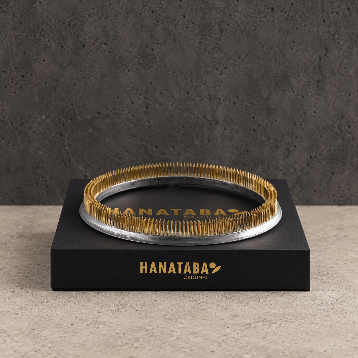 HANATABA ORIGINAL kenzan flower frog ring pin older 20cm/200 mm rests on top of a Black Box with label on a beige colored stone surface in front of a dark grey concrete wall