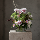 hanataba kenzan ring 150 mm in transparent acrylic material with fresh cut flowers inside a clear acrylic flower vase standing on a light beige stone piedestal against a dark grey background