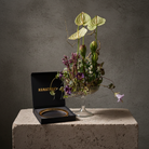 Hanataba Kenzan ring 200 mm (7 \ 7/8") flower arrangement in a glass vase piedestal staning on a stone block in front of a dark grey background