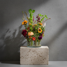 Hanataba Kenzan ring 200 mm (7 \ 7/8") floral arrangement with red and purple dahlias, sunflowers, ranuculus and greens in a glass vase on a stone block in front of a dark grey background