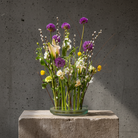 Hanataba Kenzan ring 200 mm (7 \ 7/8") flower arrangement in a rippled glass vase on a stone block in front of a dark grey background