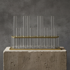 Decorative glass vase with 13 slender vases and on a concrete base against a gray wall